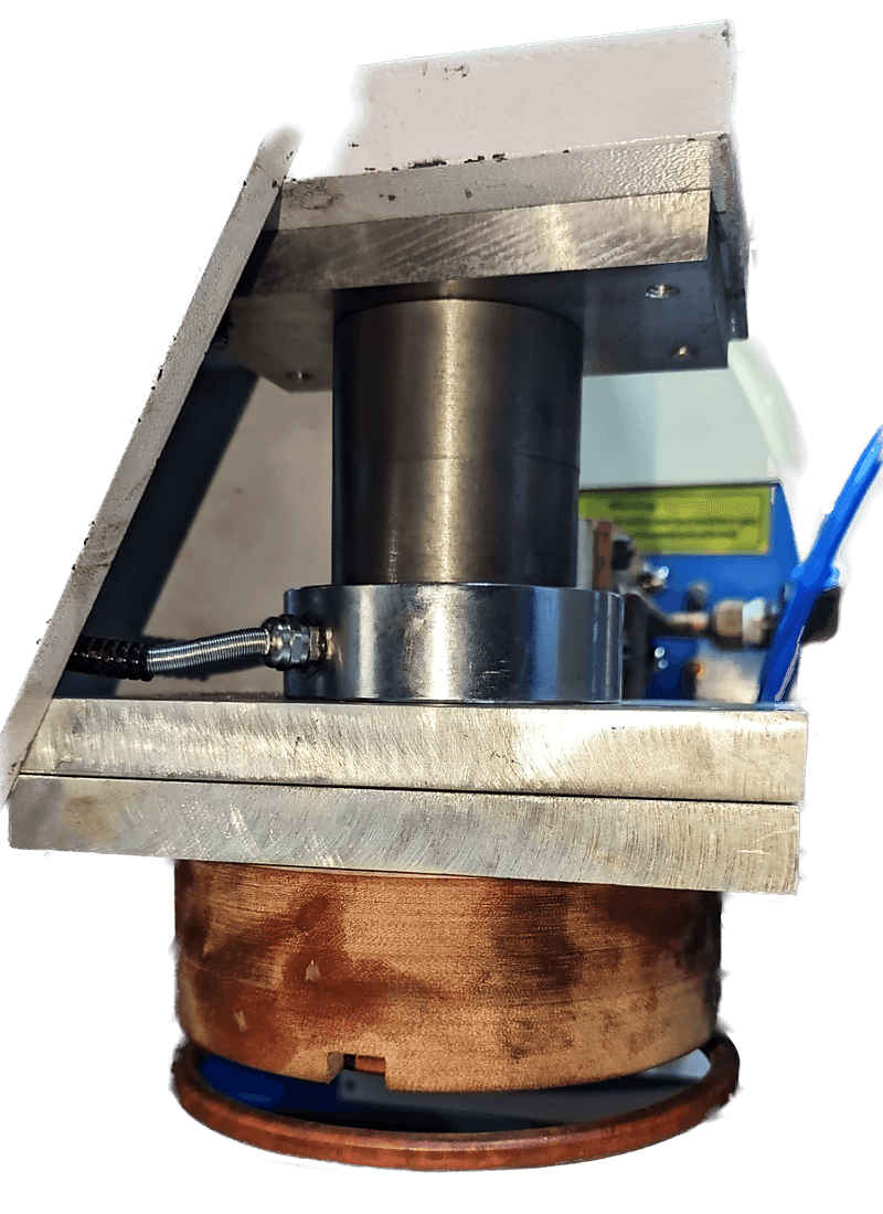 A ring inductor mounted in a machine below a fixed plate, with copper busbars and a workpiece location beneath.