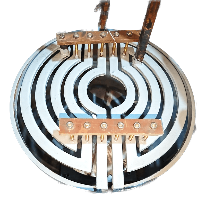 A large spiral pancake inductor built into a machine, with copper busbars and water cooling connections around the outside.