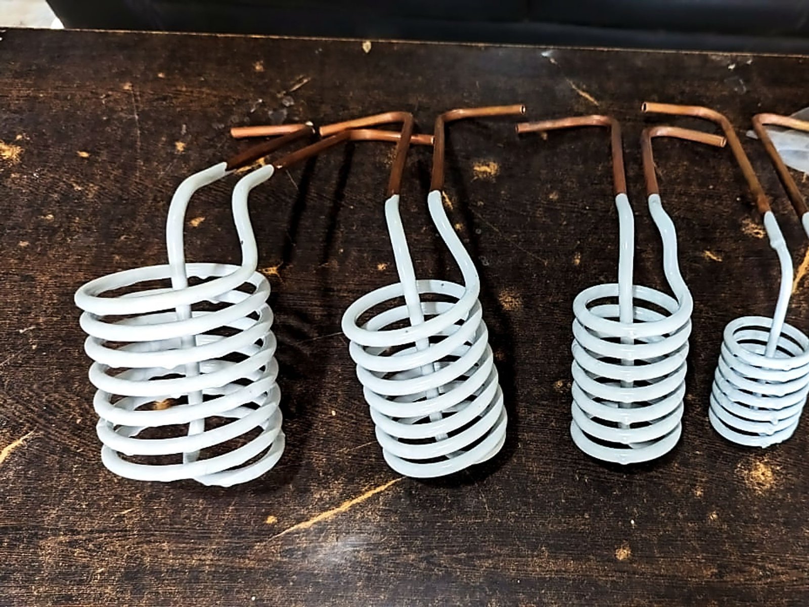 Four helical induction coils on a workbench, each wound from copper tube with white insulation between the turns and brazed connection stems.
